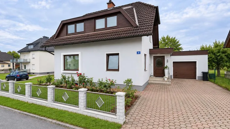 Einfamilienhaus mit gepflegtem Vorgarten, Garage und gepflasterter Auffahrt unter blauem Himmel.