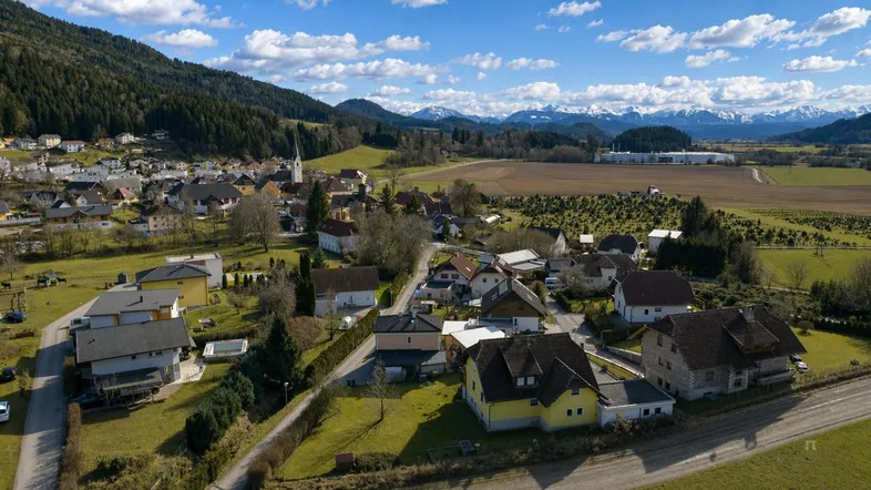 Luftaufnahme eines malerischen Dorfes mit schneebedeckten Bergen im Hintergrund unter blauem Himmel.