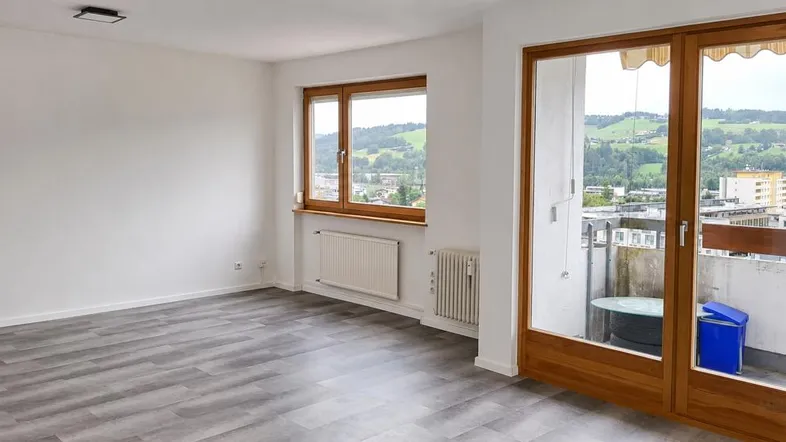 Helles Zimmer mit grauem Laminatboden, Holzbalkontür und weitem Blick ins Grüne.