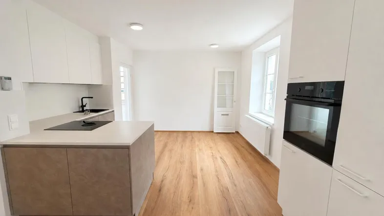 Moderne Küche mit weißen Schränken, Kochinsel und integriertem Backofen, offen zum Wohnbereich.