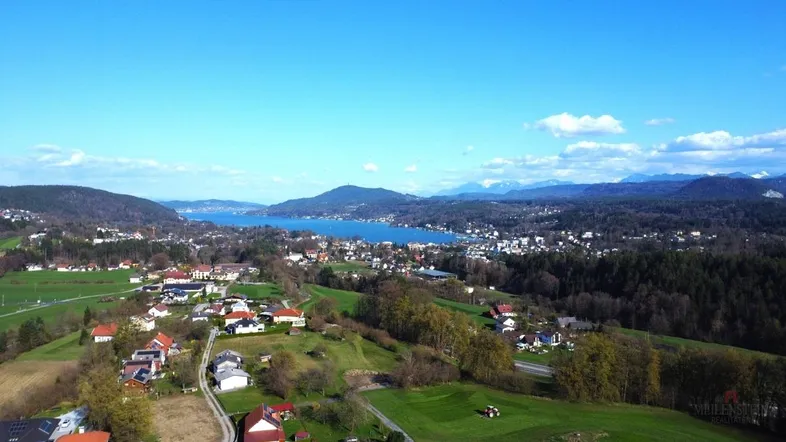 Panoramablick auf eine malerische Stadt am See mit umliegenden Hügeln und Bergen im Hintergrund.