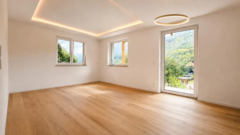 Heller, leerer Raum mit Holzboden, großen Fenstern und Bergblick, bereit für die individuelle Gestaltung.