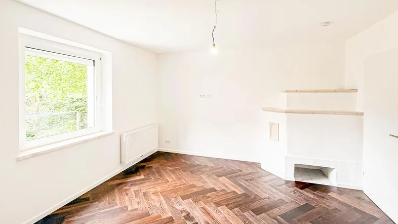 Helles Zimmer mit Fischgrätparkettboden, weiß gestrichenen Wänden und einem dekorativen Kamin.