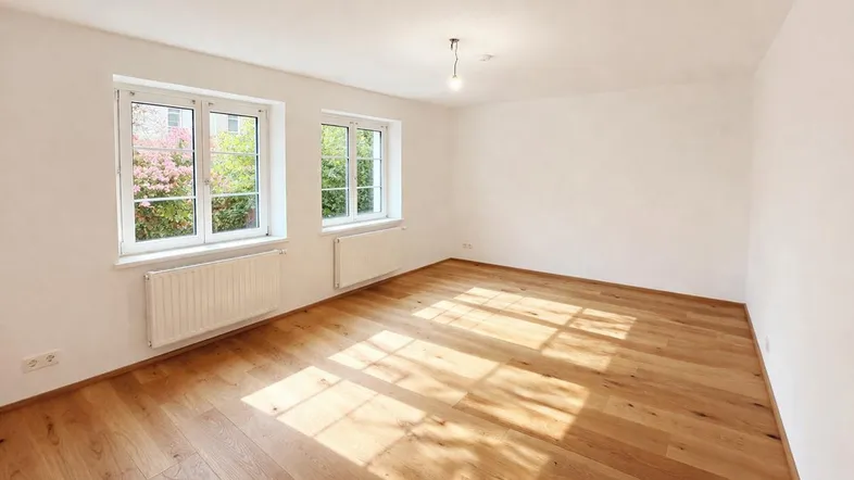 Heller Raum mit neuem Parkettboden und großen Fenstern, die viel Tageslicht hereinlassen.