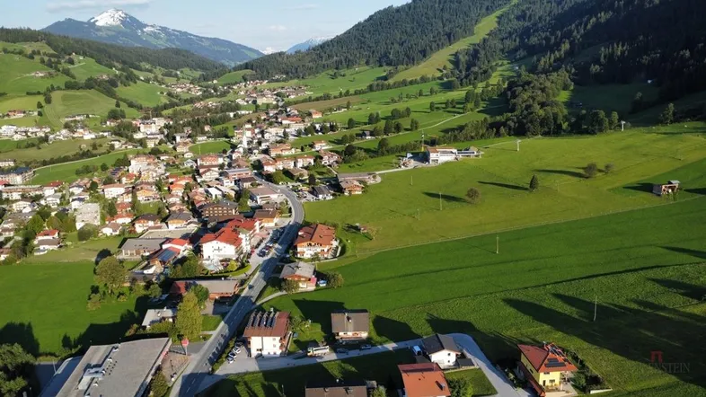 Luftaufnahme eines malerischen Dorfes in einem grünen Tal mit Bergen im Hintergrund.