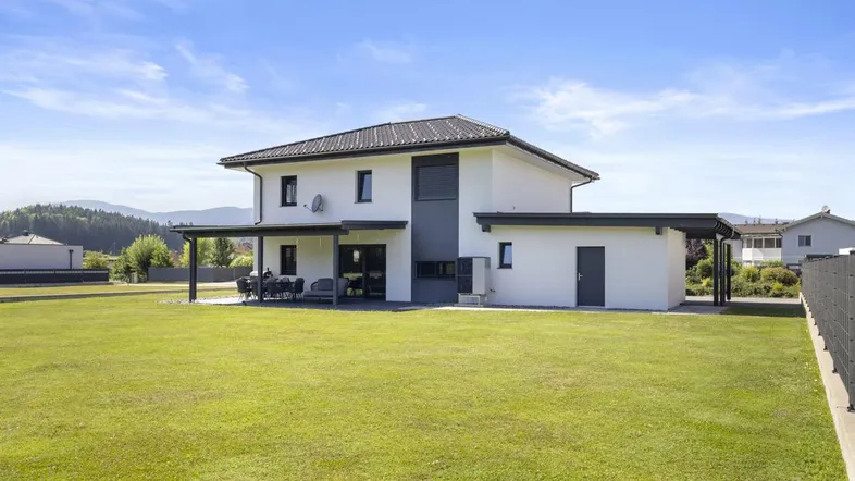 Modernes Einfamilienhaus mit großem Garten und überdachter Terrasse in ländlicher Umgebung.