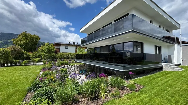 Modernes Gebäude mit mehreren Balkonen und einem gepflegten Gartenbereich unter blauem Himmel.
