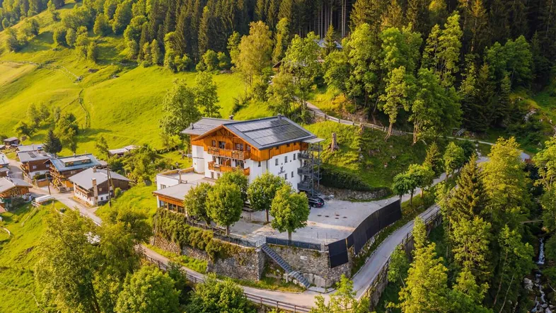 Luftaufnahme eines Gebäudes mit Solarpaneelen auf dem Dach, umgeben von grünen Hügeln und Wäldern.