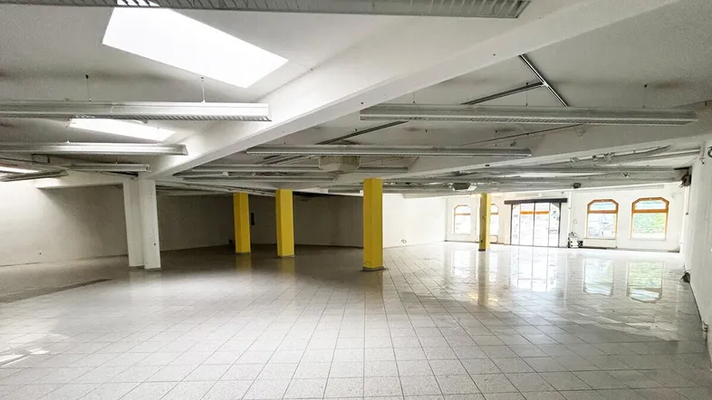 Großer, leerer Gewerberaum mit Fliesenboden, gelben Säulen und Oberlichtern, bereit für die Gestaltung.