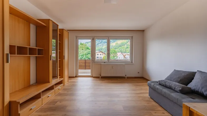 Helles Wohnzimmer mit Holzboden, Einbauschrank und Zugang zum Balkon mit Bergblick.