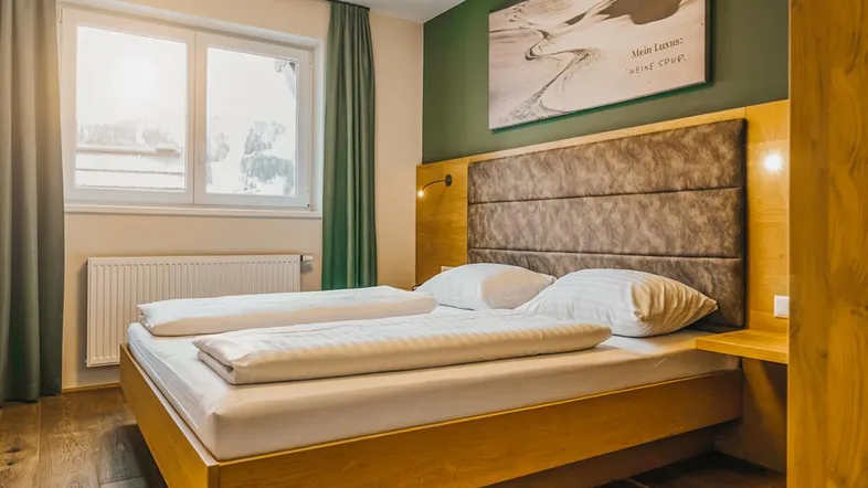 Gemütliches Schlafzimmer mit Holzboden, grüner Akzentwand und viel natürlichem Licht.