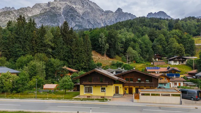 Traditionelles Haus in alpiner Umgebung mit Bergblick und umgeben von grünen Wäldern.
