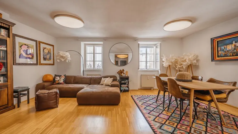 Geräumiger Wohn-Essbereich mit bequemer Couch, Esstisch und Holzboden, hell durch große Fenster.
