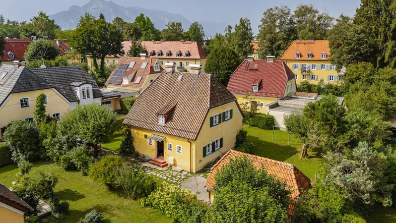 Luftaufnahme eines charmanten gelben Hauses mit Ziegeldach in einer grünen Wohngegend mit Bergblick.