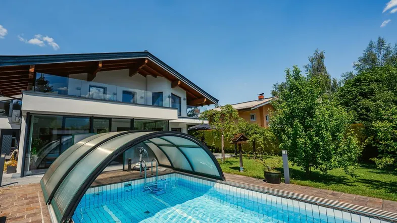 Modernes Haus mit großem Garten und überdachtem Außenpool unter blauem Himmel.