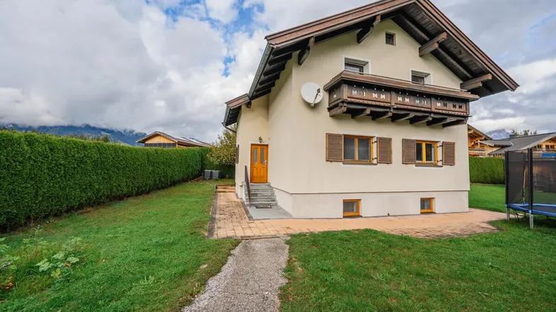 Traditionelles Haus mit gepflegtem Garten, hoher Hecke und einem Balkon mit Bergblick.