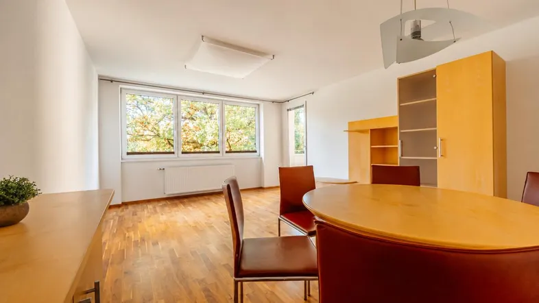 Helles Wohn- und Esszimmer mit Parkettboden, großen Fenstern und Blick ins Grüne.
