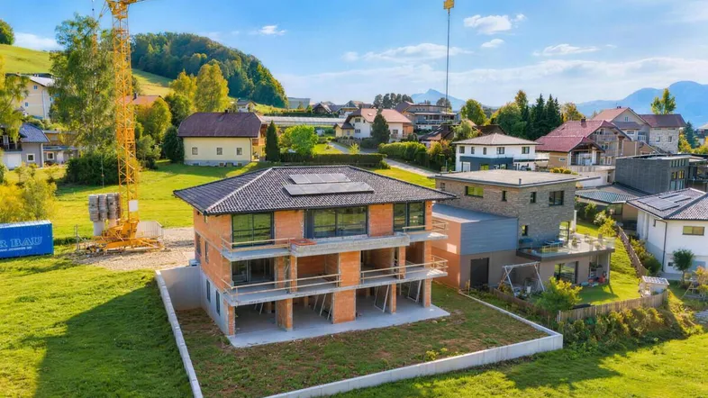 Neubau eines Mehrfamilienhauses im Rohbauzustand mit Blick auf die umliegende Hügellandschaft und Berge.