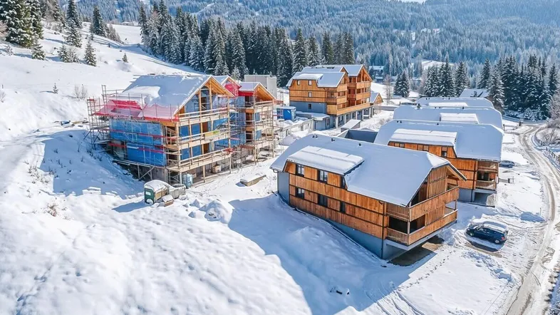 Mehrere Neubauten in einer verschneiten Berglandschaft, teilweise noch im Bau.