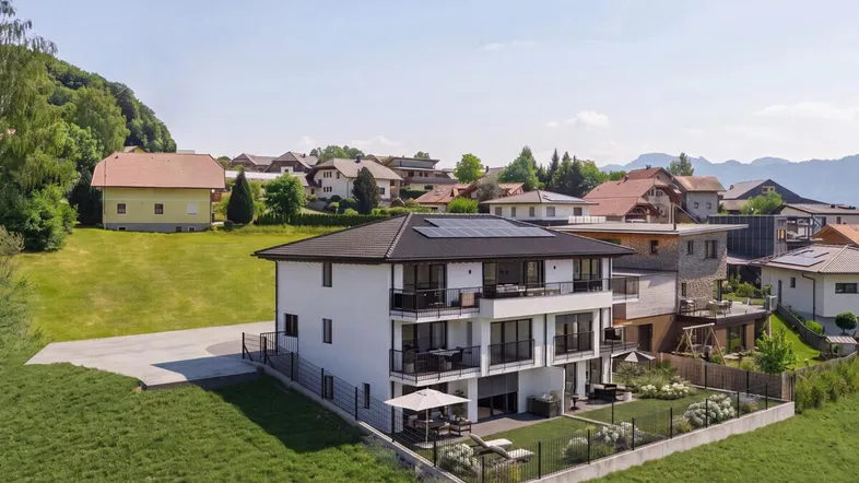 Modernes Mehrfamilienhaus mit Balkonen, Terrassen und Garten in ländlicher Umgebung mit Bergblick.