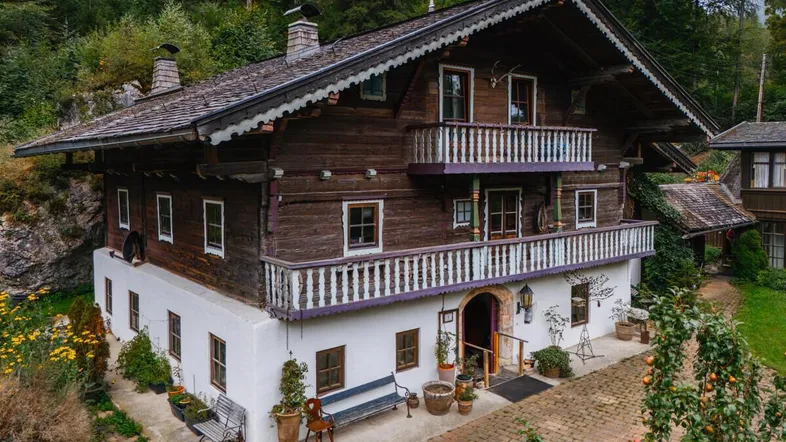 Traditionelles alpenländisches Haus mit Holzbalkonen und weiß getünchter Fassade, umgeben von Natur.