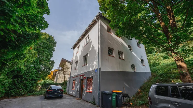 Außenansicht eines Mehrfamilienhauses mit Parkplätzen und umgebender grüner Vegetation.