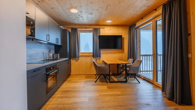 Moderner Wohn-Essbereich mit integrierter Küche, Holzwänden und Zugang zum Balkon.