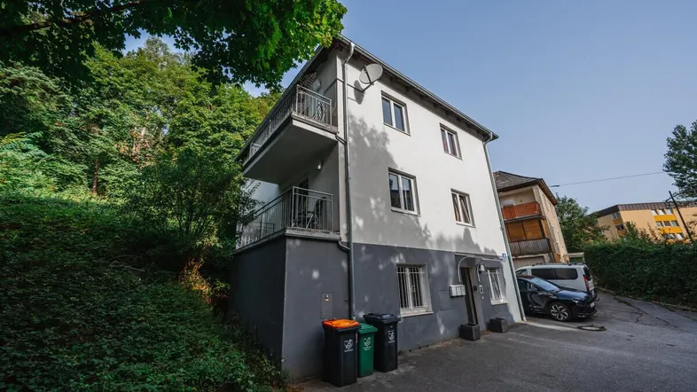 Mehrstöckiges Wohnhaus mit Balkonen und Parkplätzen, umgeben von viel Grün.