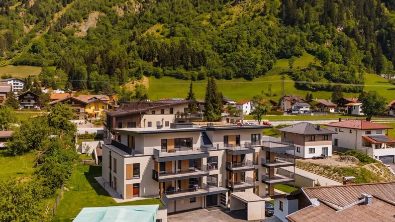 Moderne Wohnanlage in alpiner Landschaft mit Bergblick und Balkonen unter grün bewachsenen Hängen.