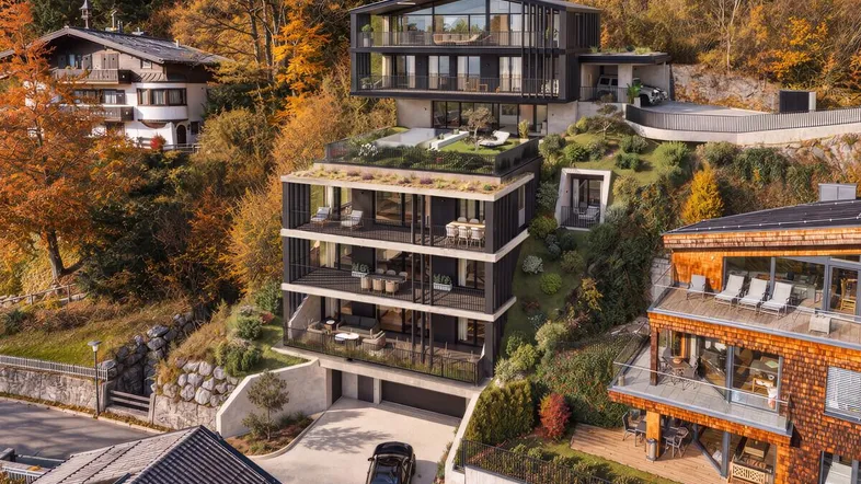 Moderne Terrassenhäuser in Hanglage mit großen Glasfronten und herbstlicher Umgebung.
