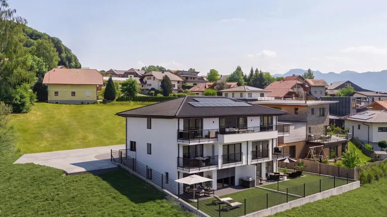 Modernes Mehrfamilienhaus mit mehreren Balkonen und Terrassen in ländlicher Umgebung mit Bergblick.