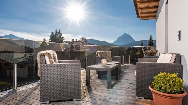 Sonnige Terrasse mit Holzboden, modernen Loungemöbeln und weitem Bergblick.