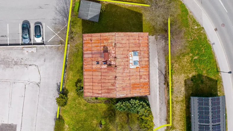 Luftaufnahme eines Grundstücks mit Haus, Nebengebäude und angrenzendem Parkplatz, umrandet von einer gelben Linie.