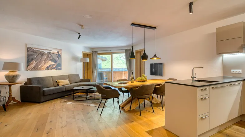 Geräumiger offener Wohn- und Essbereich mit moderner Küche, Holzboden und Zugang zum Balkon mit Bergblick.