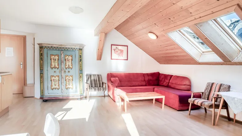 Helles Wohnzimmer im Dachgeschoss mit Holzbalken, gemütlichem Sofa und traditionellem Schrank.