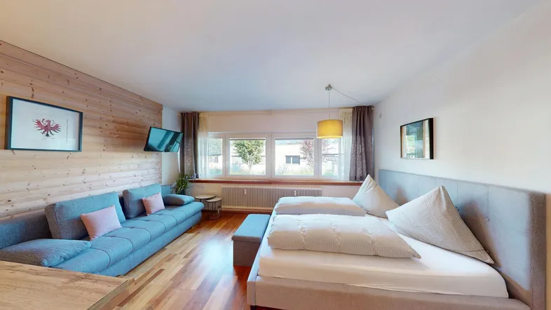 Helles Wohnzimmer mit Holzwand, bequemer Couch und Doppelbett, ideal für Entspannung.