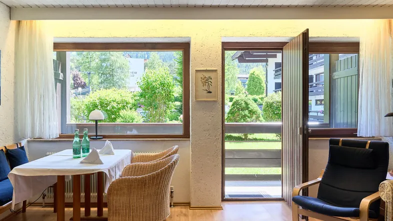 Helles Wohn- und Esszimmer mit Holzboden, gemütlichen Möbeln und Zugang zum Balkon mit Blick ins Grüne.