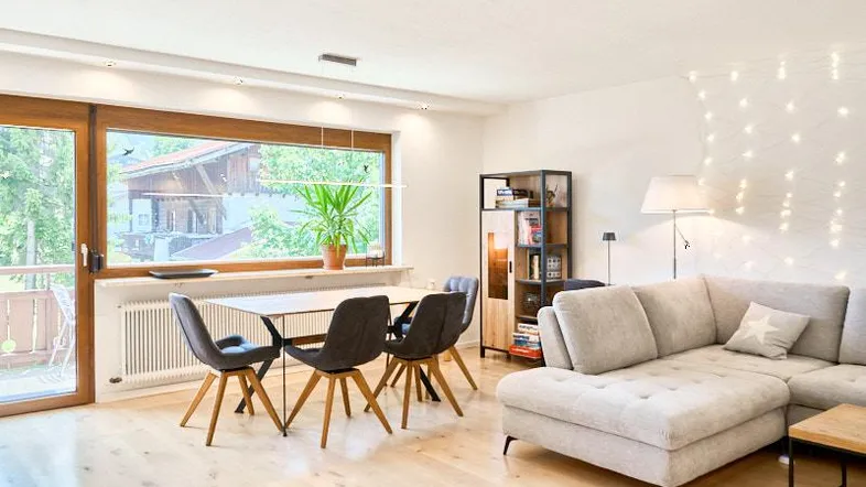 Helles Wohn- und Esszimmer mit Holzboden, großem Fenster und Zugang zum Balkon.