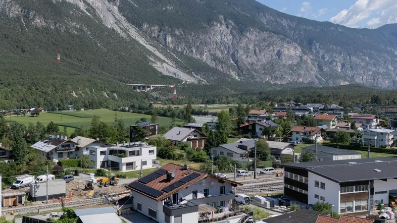 Panoramablick auf eine Wohnsiedlung mit Bergen im Hintergrund und einem Tal.