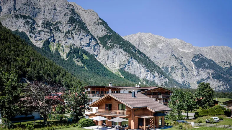 Holzhaus in alpiner Landschaft mit majestätischen Bergen im Hintergrund und sonniger Terrasse.