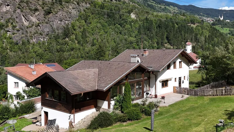 Traditionelles Haus in alpiner Landschaft mit Satteldach und großem Garten, umgeben von grünen Hügeln.