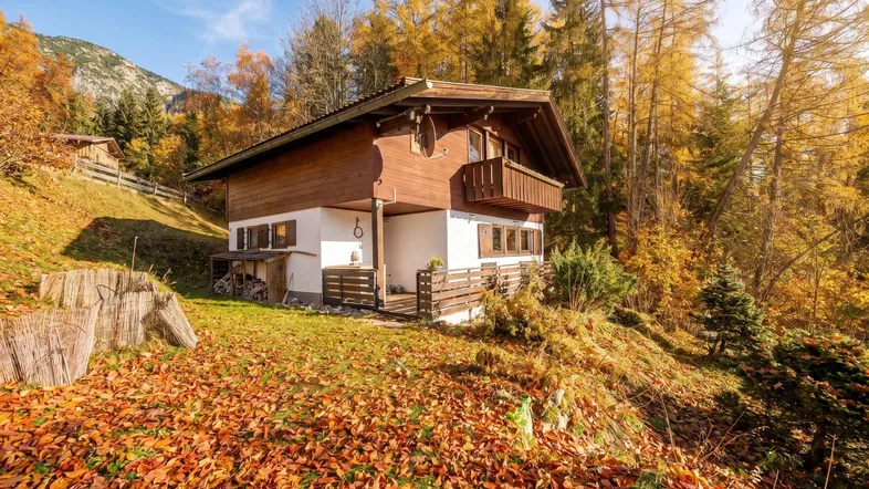 Charmantes Holzhaus in alpiner Umgebung, umgeben von herbstlicher Natur und Bergen.