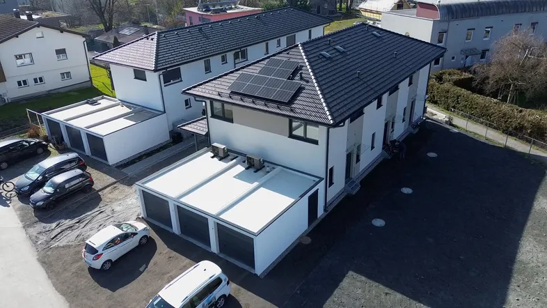 Neubau mit Photovoltaikanlage auf dem Dach und Garagen im Vordergrund, umgeben von Grünflächen.