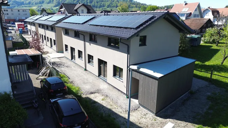 Reihenhäuser mit moderner Architektur und Photovoltaikanlagen auf den Dächern in ländlicher Umgebung.