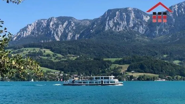 Panoramablick auf einen malerischen See mit majestätischen Bergen im Hintergrund und einem Schiff auf dem Wasser.