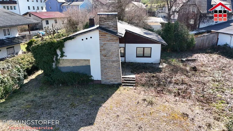 Ansicht des Einfamilienhauses mit Steinkamin und verwildertem Gartenbereich in ländlicher Umgebung.