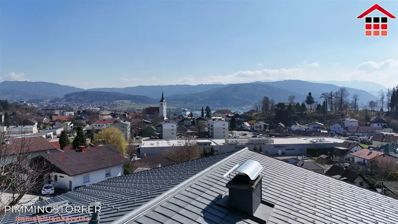 Panoramablick über eine Stadt mit Bergen und einem See im Hintergrund, aufgenommen von einem Dach.