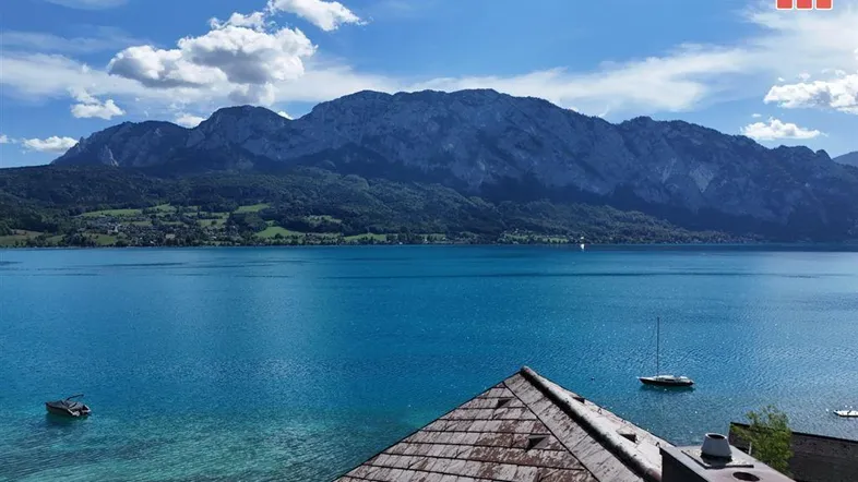Atemberaubender Blick auf den See und die umliegenden Berge unter blauem Himmel mit Wolken.