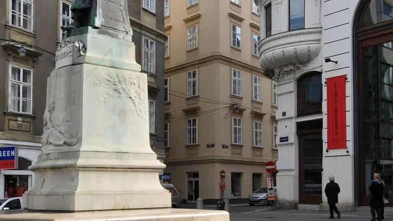 Historische Gebäude und eine Statue prägen das Stadtbild dieser belebten Wiener Straße.