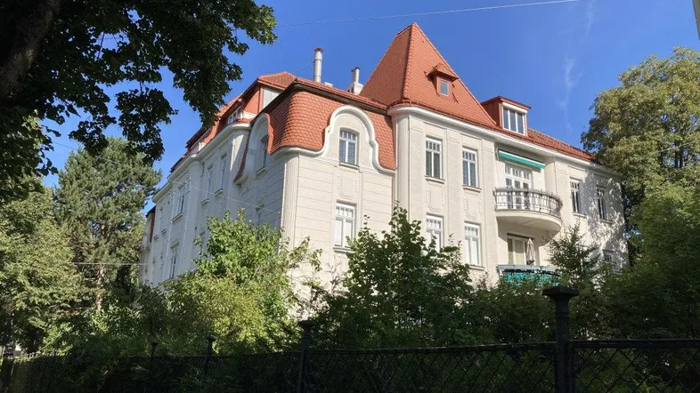 Großes, elegantes Gebäude mit rotem Mansarddach und klassischer Architektur, umgeben von Bäumen.